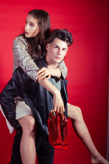 young pretty guy and girl closed in fashion style after party shoes in hand posing on red background, lifestyle people concept