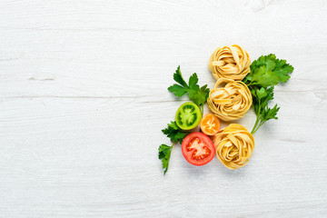 Dry pasta, tomatoes, greens, oil and ingredients. Italian traditional cuisine. Fresh vegetables. Top view. Free space for your text.