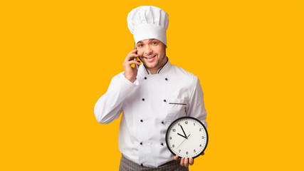 Professional Cook Talking On Phone Holding Clock Standing In Studio