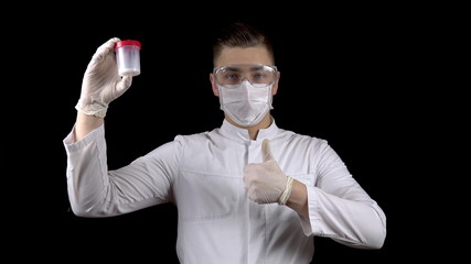 Young man doctor checks sperm tests. A man examines a test jar, then shows a thumb up. Positive semen analysis. On a black background. - obrazy, fototapety, plakaty