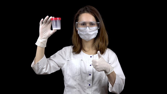 Young woman doctor checks sperm tests. A woman examines a test jar, then shows a thumb up. Positive semen analysis. On a black background.