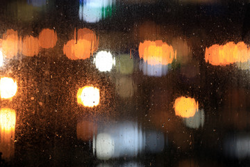 Rain Drops Falling on window with bokeh light effects in the background. Heavy rain falling on glass surface. Raindrops trickle down. Rainfall, Drip, Raining, Droplets of water.