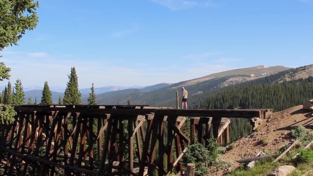 man walking across decrepit trestle bridge in colorado. Stationary, handheld