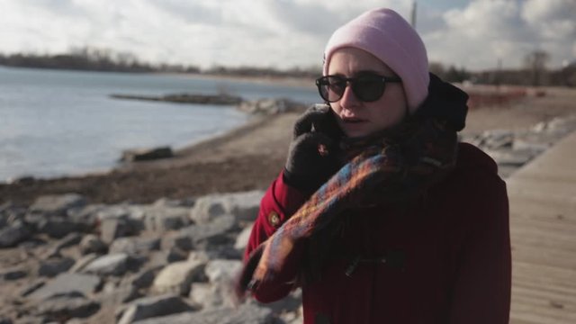 Canada - Beautiful Woman Talking With Someone On Her Phone While Walking Near The Rocky Sea Shore On A Windy Day - Closeup Shot