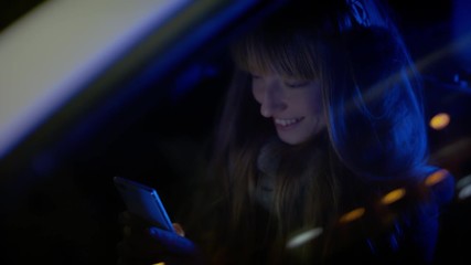 Woman smiling and texting inside her car on a cold evening.