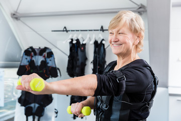 Senior lady staying fit with dumbbell exercise in wireless ems gym - obrazy, fototapety, plakaty