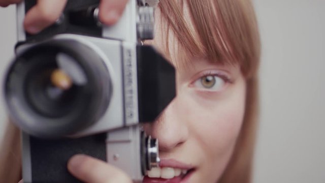 Female photographer behind DSLR camera reveals face sideway and smile, Close up