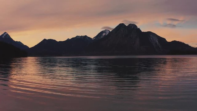 Anamorphic 4K Aerial Drone footage of a young couple standing at the shore of the famous and scenic and idyllic Bavarian lake Walchensee in southern Germany in the alps by sunset.