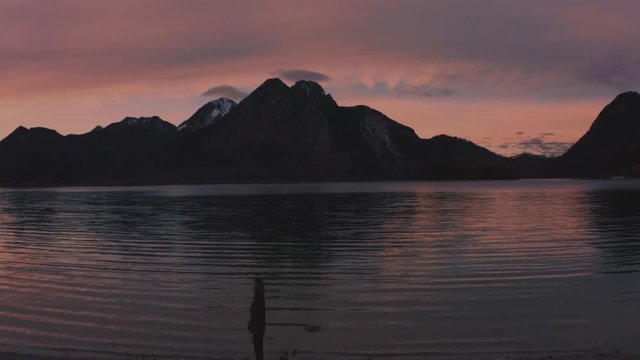 Anamorphic 4K wide aerial Drone footage of a young German woman standing at the shore of the famous and scenic and idyllic Bavarian lake Walchensee in southern Germany in the alps by sunset.