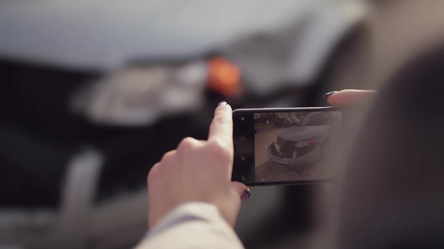 Woman takes a photo on her smartphone after crash of a broken car. Tracking shot, panning right.