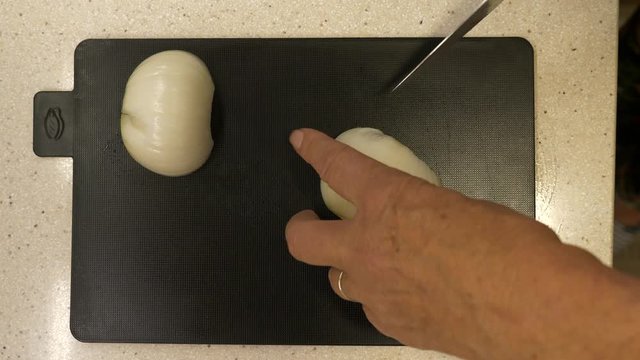 Slicing white onions with a stainless steel knife on a black chopping board - Top view