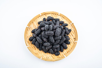 A bamboo dish filled with fresh black mulberries on a white background