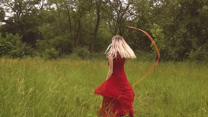 Cute young woman with blonde hair dances through the meadows. In this dreamlike shot she wears a red dress and playfully twirls around a ribbon wand. - Powered by Adobe