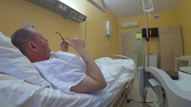 The patient is communicates with a smartphone chromakey green. A man wears glasses lifting the headboard of the bed and picks up a smartphone with a green screen.