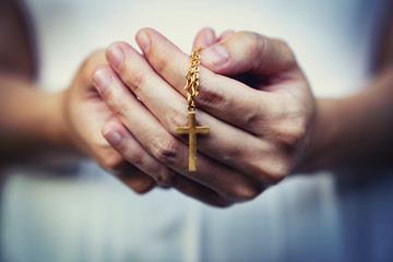 woman hands praying holding a beads rosary with Jesus Christ in the cross or Crucifix on black...