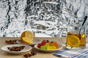 Marmalade jelly candies, lemon, star anise on a ceramic plate on a surface of rough and old paper. Tea in a cup. View from above.