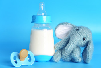 Bottle of milk for baby and toy with pacifier on color background