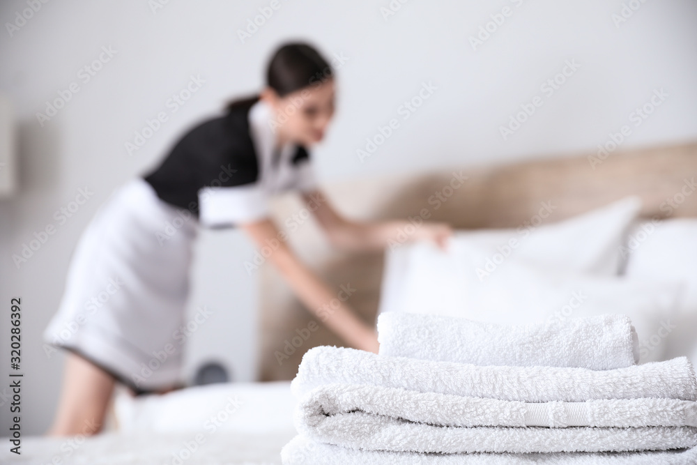 Sticker Beautiful chambermaid making bed in hotel room, focus on towels