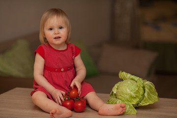 Fototapeta premium cute little girl is a vegetarian, eating vegetables cabbage and tomatoes in the kitchen in a red dress. Concept: healthy food, diet, vegetarianism. Vegan food.
