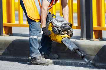 Worker with pneumatic demolition hammer breaking asphalt at road construction site. Man drilling and repairing concrete driveway surface with plugger hammer. Road repairing works with jackhammer