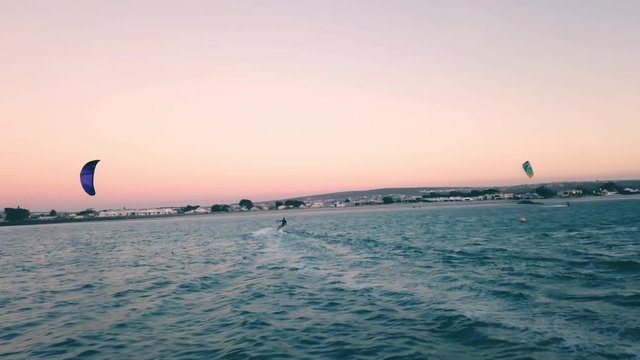 ultra-wide powerful action drone shot chasing a kite surfer on full speed during sunset on Langebaan Beach, Cape Town, South Africa with summer vacation silhouette.