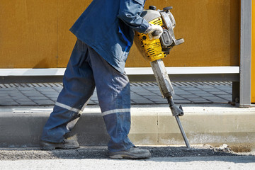 Worker with pneumatic demolition hammer breaking asphalt at road construction site. Man drilling and repairing concrete driveway surface with plugger hammer. Road repairing works with jackhammer