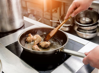 Chef cooks fried potatoes with pieces of meat in a restaurant kitchen