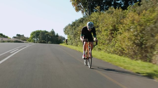 Tracking Shot of a Young Male Road Cyclist Racing Down a Hill