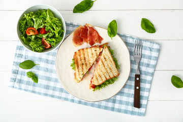 Plate with tasty sandwiches and vegetable salad on table