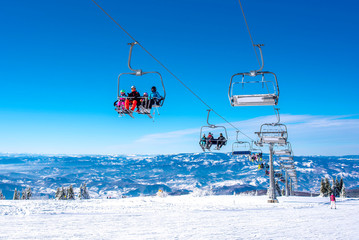 Skiers on ski lift at mountain ski resort with beautiful sky and mountains in the background - obrazy, fototapety, plakaty
