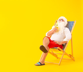 Santa Claus with cocktail sitting on sun lounger against color background. Concept of vacation