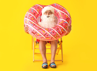 Santa Claus with swimming ring sitting on sun lounger against color background. Concept of vacation
