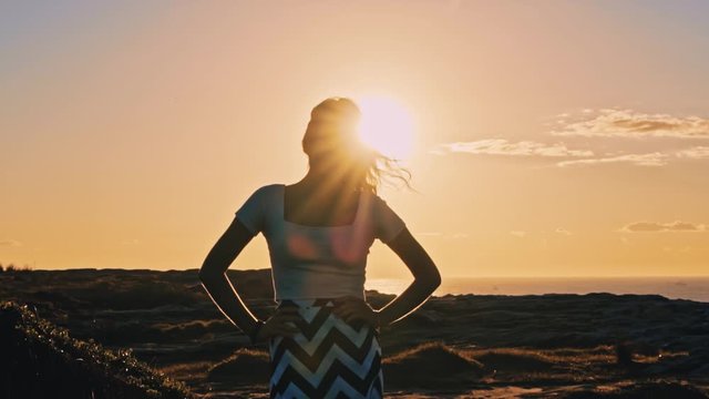 Pretty Model Standing On The Grassy Hills While Looking At The Camera With Beautiful Sunset in The Background in Australia - Wide Shot 