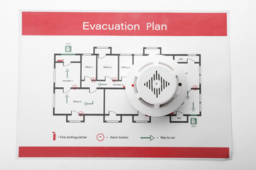 Evacuation plan and smoke detector on white background