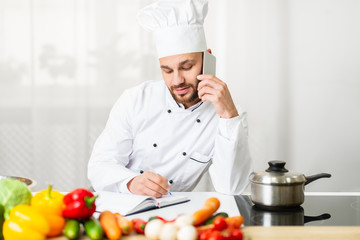 Chef Talking On Phone Receiving Order Standing In Hotel Kitchen