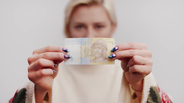 Close up shot of the Banknote Of One Ukrainian Hryvnia in the hands of a blonde woman. soft selective focus, head and shoulders portrait