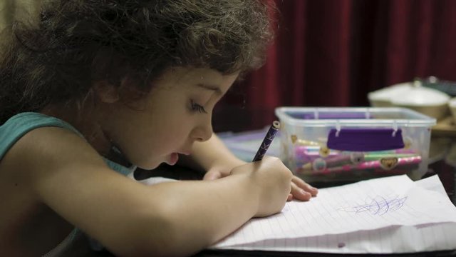 Little girl drawing a picture on notebook paper with colored pencils sitting at a desk