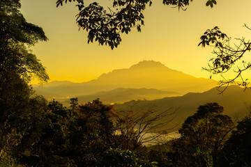 The mount Kinabalu and layers of hills with golden light, being framed with foliages