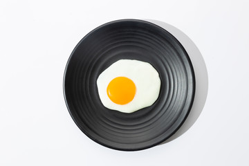 Fried egg on black plate on  white background.