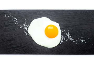 Fried egg on slate plate with salt on white background. Cooking and food concept.