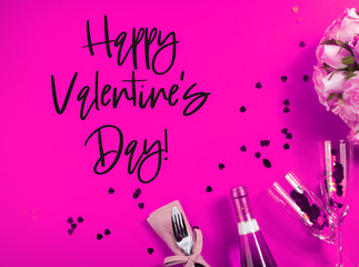Romantic dinner concept flat lay on pink background with heart confetti, rose flowers, festive napkin tableware and champagne flutes and bottle. Greeting card with Happy Valentines day text