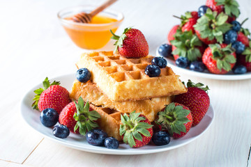 Fresh homemade food of berry Belgian waffles with honey, chocolate, strawberry, blueberry, maple syrup and cream. Healthy dessert breakfast concept with juice