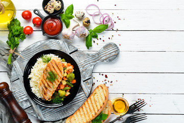 Baked chicken fillet with rice and vegetables on a black plate. Top view. Free copy space.