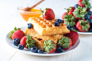 Fresh homemade food of berry Belgian waffles with honey, chocolate, strawberry, blueberry, maple syrup and cream. Healthy dessert breakfast concept with juice