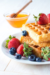Fresh homemade food of berry Belgian waffles with honey, chocolate, strawberry, blueberry, maple syrup and cream. Healthy dessert breakfast concept with juice