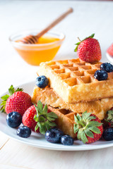 Fresh homemade food of berry Belgian waffles with honey, chocolate, strawberry, blueberry, maple syrup and cream. Healthy dessert breakfast concept with juice