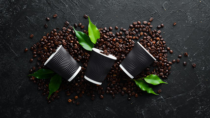 Paper cups for coffee and coffee beans. On a black stone background. Top view. Free space for your...