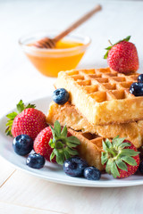 Fresh homemade food of berry Belgian waffles with honey, chocolate, strawberry, blueberry, maple syrup and cream. Healthy dessert breakfast concept with juice