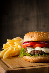 Home made hamburger with beef, onion, tomato, lettuce and cheese. Fresh burger close up on wooden rustic table with potato fries, beer and chips. Cheeseburger.