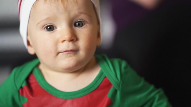 Adorable baby boy with big bright eyes in cute elf costume for Christmas. Close up view of face of child. Slow motion, hand held scene with toddler in holiday pajamas.